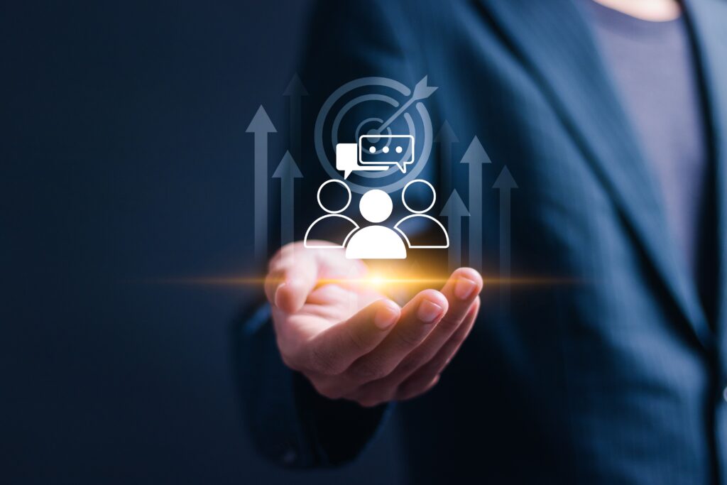 Closeup of a hand held palm-up. Three simplified images of people, looking like Chess pawns, are hovering above it with an archery target and upward-pointing arrows.