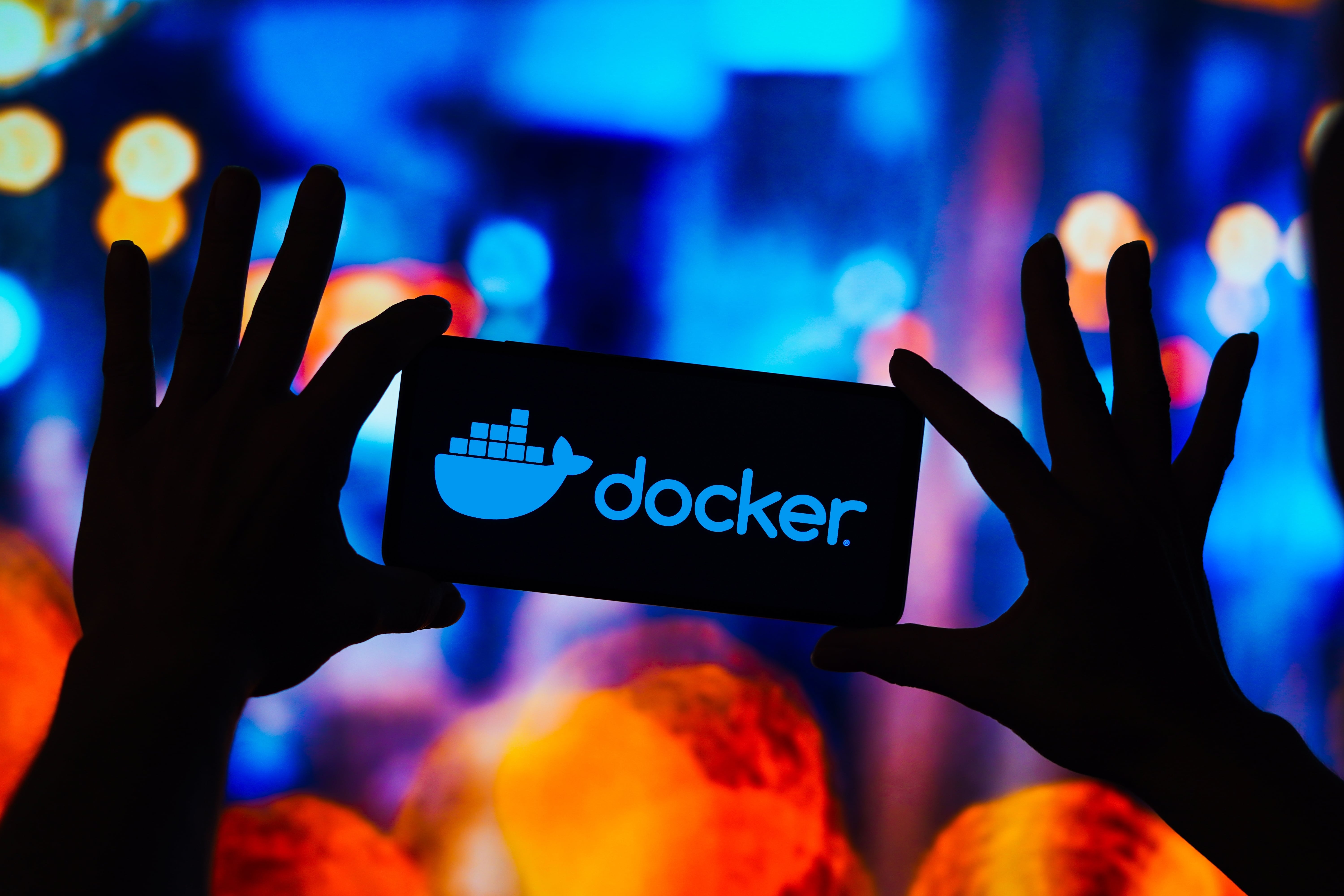 Two hands in silhouette holding a placard that shows the Docker logo and name as if light from behind it is passing through.