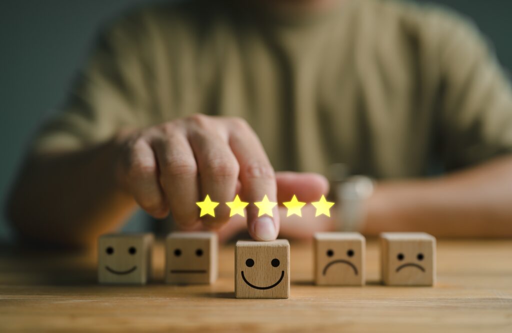 Person choosing a block from among five that have different, simple faces with two eyes and a mouth to indicate emotion. The center one, which is chosen, is smiling and there are five gold stars above it.