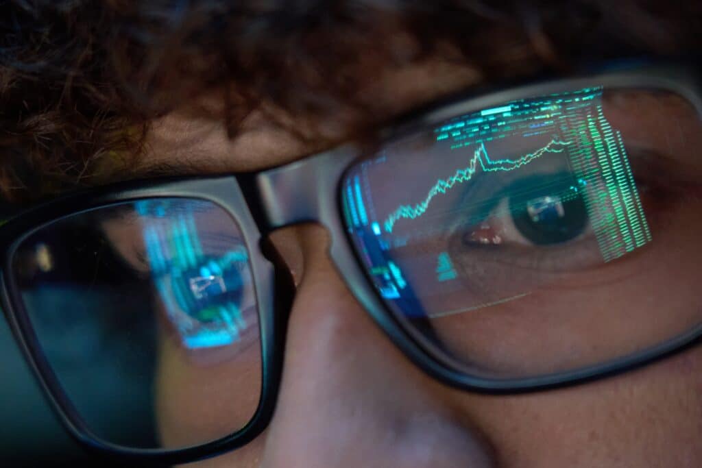 Closeup of a young man's eyes. There is a screen reflected in his glasses.